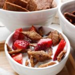 Homemade cereal in a small bowl with a few cut up strawberries and plant milk