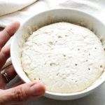 Hand beside small bowl of gluten-free sourdough starter.