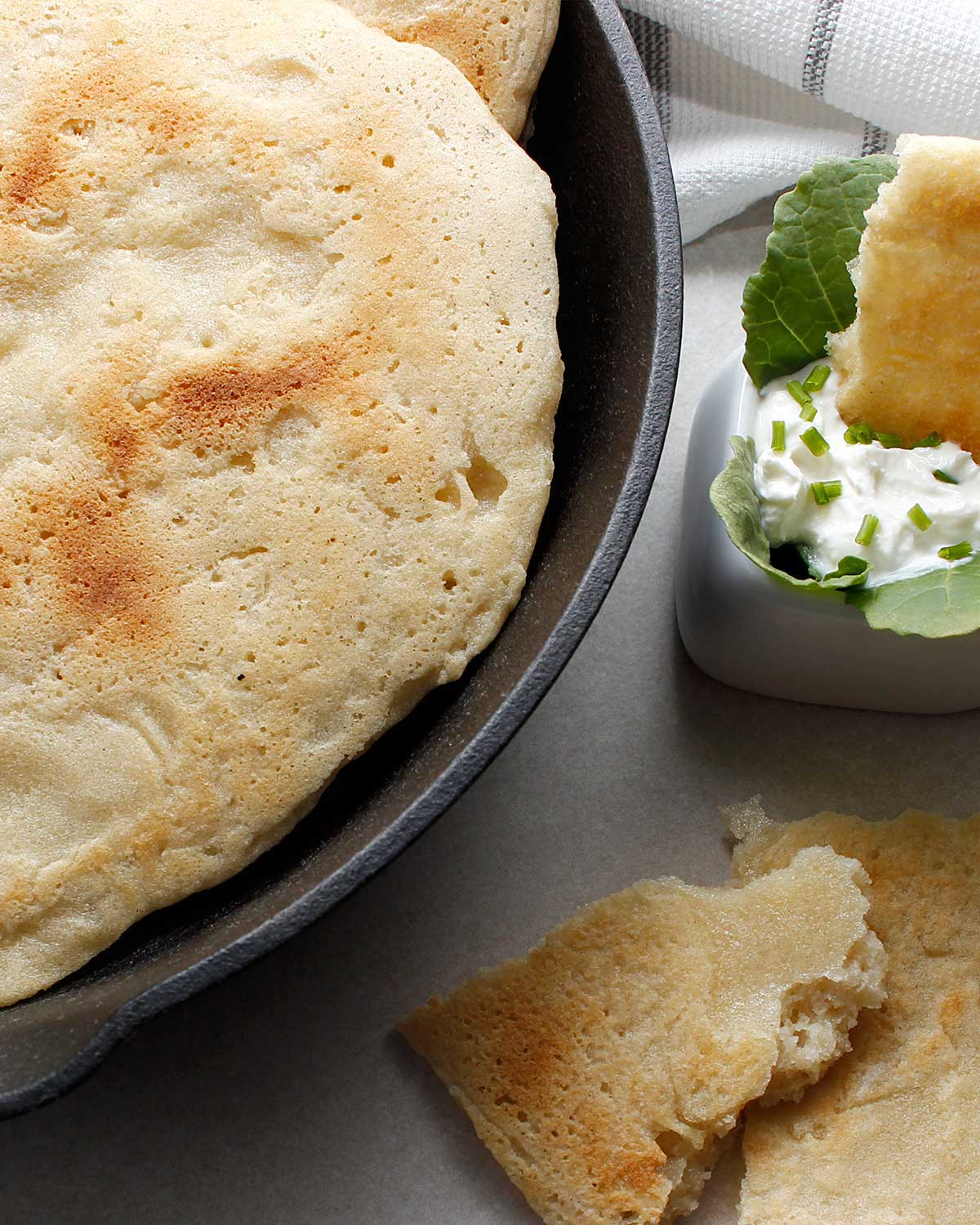 Gluten-free sourdough naan bread in a skillet with pieces on the side with one dipped in a white garlic dip.