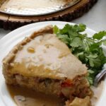 Slice of vegetable pot pie with a generous serving of homemade vegan gravy.