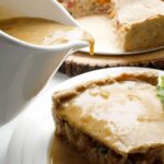 Pouring GF vegan gravy over a slice of vegetable pot pie.